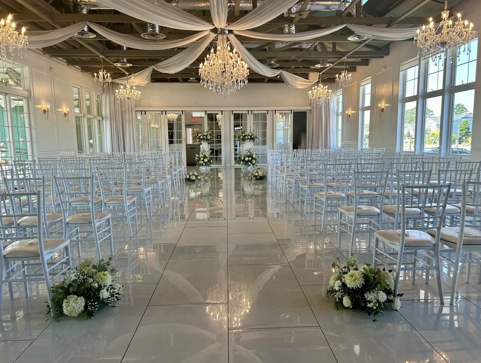 Bright ceremony hall with chandeliers, draped ceiling, and white floral markers