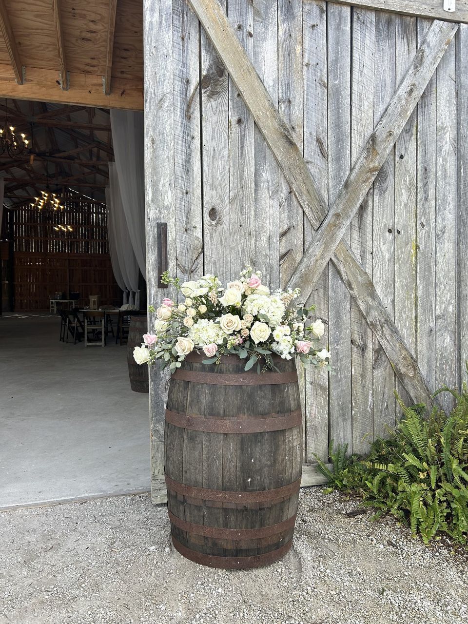 Barrel arrangement with white and blush roses at a rustic barn entrance