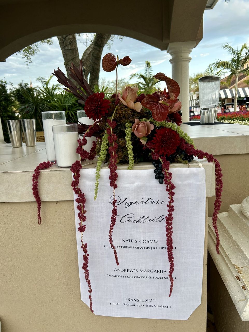 Burgundy floral arrangement crowning a signature cocktails sign